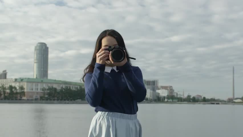 Young woman photographer holding a DSLR camera, taking photos, with focus on lens and creative composition in a professional photography setting.