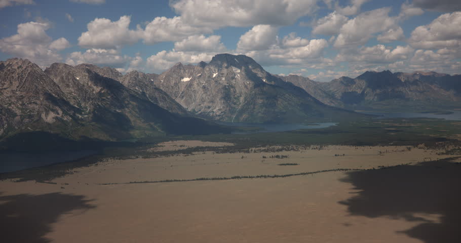 Aerial summer footage of Bradley Lake and Taggart Lake set against the dramatic peaks of the Grand Teton Mountains in Grand Teton National Park, Wyoming. Clear weather highlights alpine lakes, rugged mountain terrain, and pristine wilderness in this scenic Western United States landscape. Ideal for travel, tourism, nature, conservation, and outdoor adventure content.
