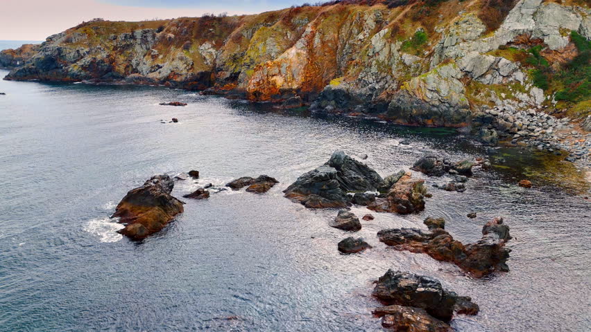 Jagged coastal rocks and cliffs at the sea edge. High angle view of complex rocky formations and cliffs along the shoreline with clear sea water.