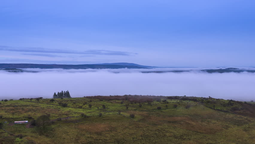 Timelapse of rural landscape with fog inversion rolling above lake in distance and hills beyond viewed from Carrowkeel in county Sligo in Ireland.