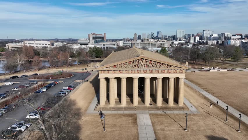 Aerial drone view of Parthenon in Nashville, Tennessee with downtown skyline rising in the background, showing Centennial Park and city’s modern architecture on a clear day. Wide shot.
