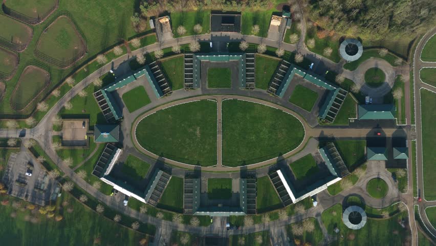 Cinematic drone perspective of the famous Newmarket gallops and elite racing yards in England featuring thoroughbred mares and future champions.