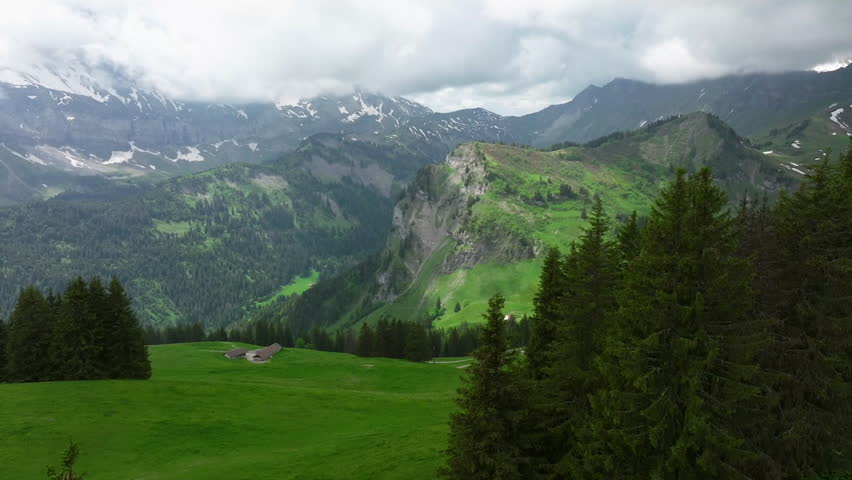 A panoramic view of a lush green mountain landscape featuring rolling hills and rocky peaks under a cloudy sky. The scene captures the tranquility of nature with a hint of dramatic weather.