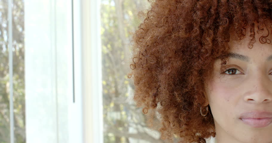 African American woman standing by curtains with sunlight filtering, blinking, smiling, copy space. Portrait, serenity, natural light, elegance, wellness, interior, relaxation