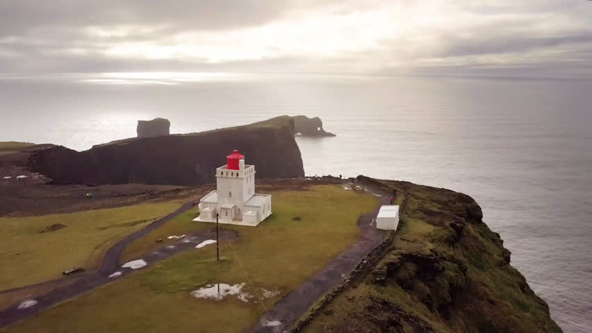 An aerial shot captures a scenic view of coastal rock formations and a lighthouse overlooking the ocean. The serene landscape showcases the natural beauty of the shoreline.