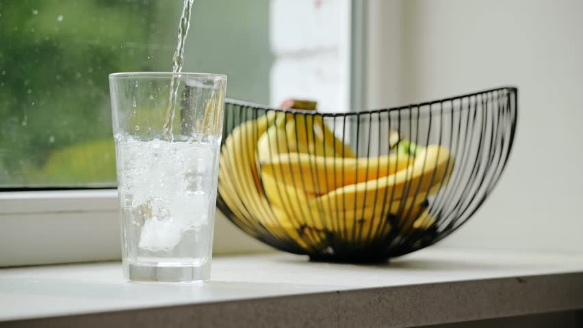 Slow motion shot of ice water poured beside bananas on cloudy day window
