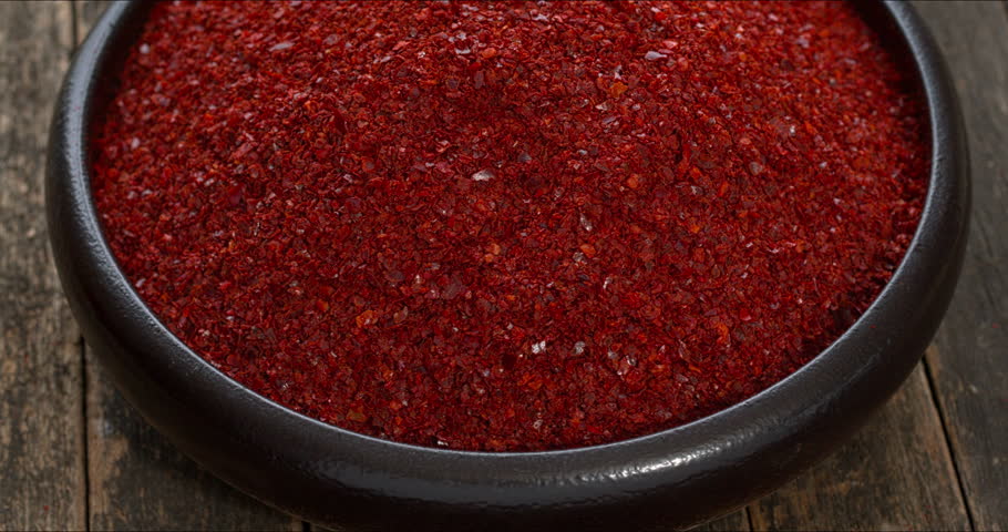 A bowl of gochugaru, Korean red chilli pepper flakes, rotating on a rustic wooden background.