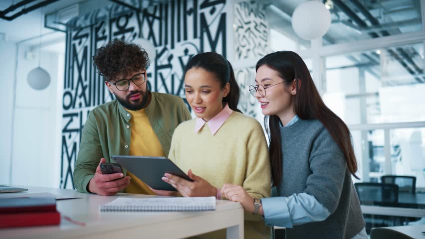 Bright room in modern office setting. Colleagues gathering around tablet and discussing problem with application. Man pointing at screen while woman explaining. Team cooperating and troubleshooting.