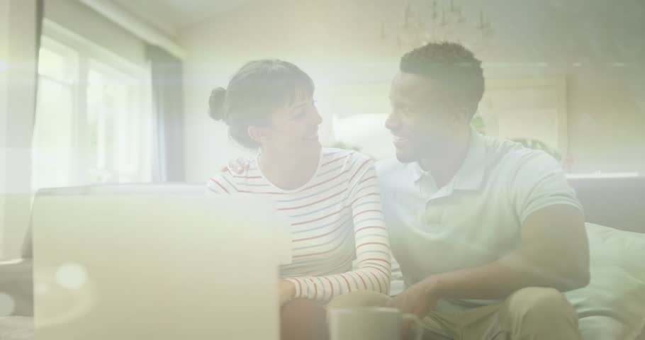 Couple on sofa viewing laptop showing HAPPY ST PATRICKS DAY confetti obscuring them, for marketing. Festive, green, overlay, livingroom, duo, mug, daylight