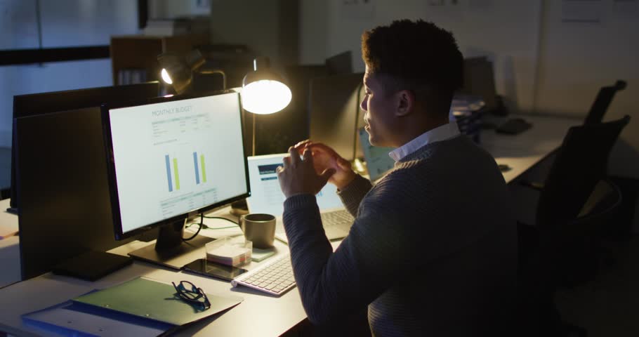 Male finance analyst leaning at desk, getting like alerts overlaying charts, rising then fading. Notifications, overload, stress, office, night, workspace, data