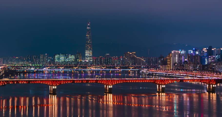 Timelapse unveils illuminated Seongsu Bridge in red lights with prominent Lotte World Tower piercing Seoul skyline amid Han River reflections and surrounding high-rise city glow
