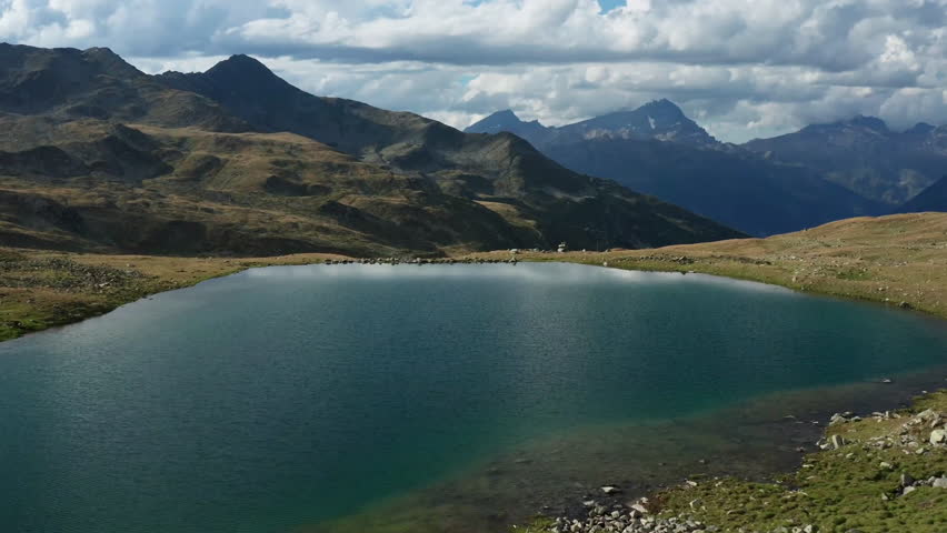 A tranquil mountain lake surrounded by rugged terrain and peaks, with clouds reflecting on the water