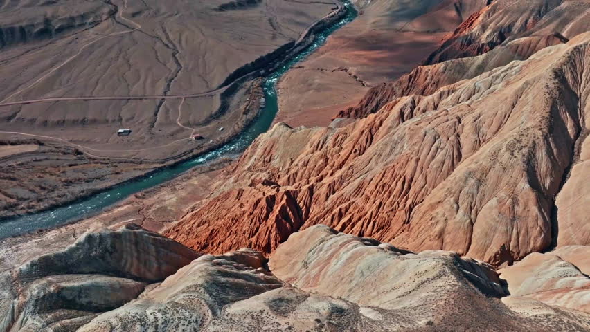 This clip showcases an aerial perspective of vibrant mountain formations alongside a winding river, highlighting the natural beauty of the terrain.