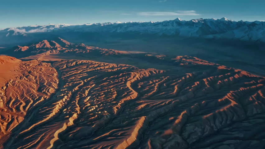This clip showcases a stunning aerial view of a rugged mountain landscape illuminated by the warm glow of sunset. The intricate patterns of the terrain create a mesmerizing visual effect.