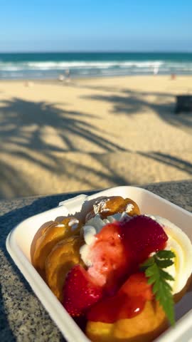 Cream puffs dessert with fresh strawberries and whipped cream, enjoying a sweet treat at the beach while relaxing under tropical palm tree shadows on a sunny summer day