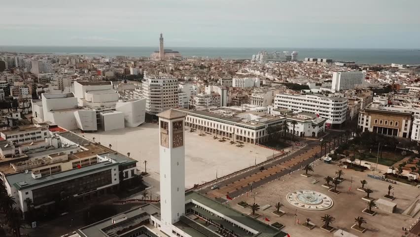 Panoramic aerial drone shot capturing the grand administrative square of Casablanca. Features the modern Grand Theatre architecture, the historic city hall, and the distant Atlantic skyline.