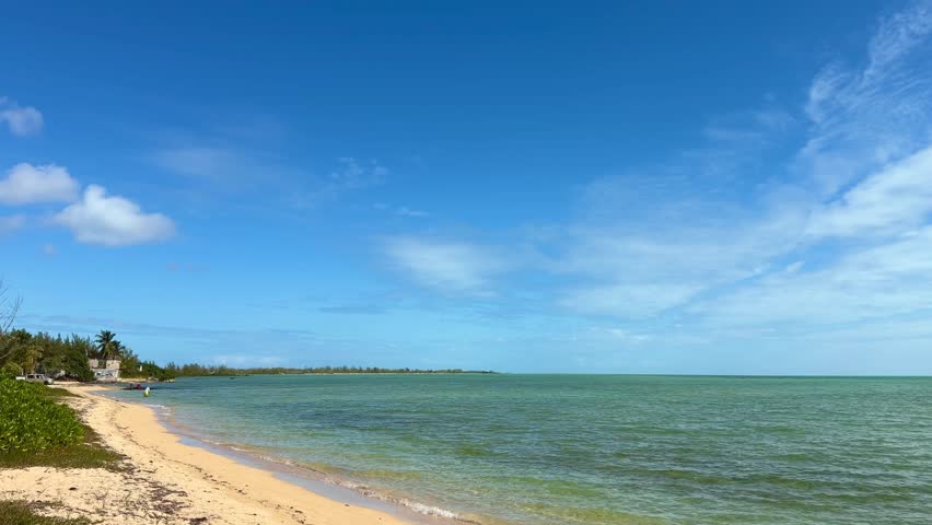Nassau beach with clear turquoise water lapping white sand beneath a bright blue sky, a tranquil, sunlit Caribbean shoreline perfect for a peaceful tropical getaway