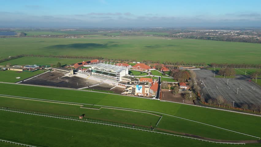 Wide drone shot of the Newmarket Racecourse grandstands and turf track in England on a sunny winter day capturing the home of British horse racing.