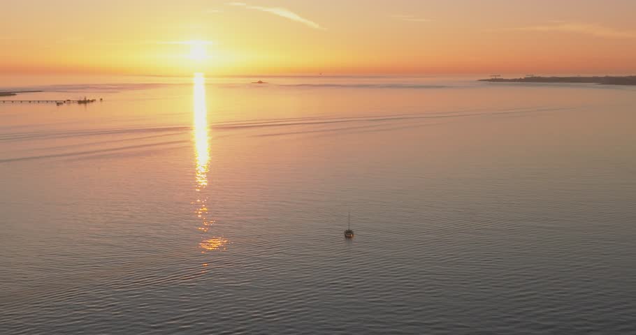 Tagus River in Lisbon with boats beneath glowing sun at sunset, aerial drone wide shot, Portugal