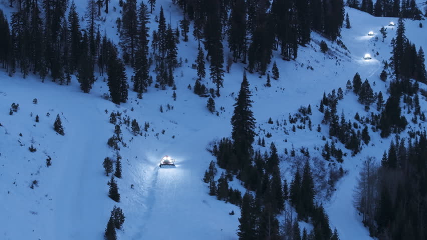 Top down aerial view of snowcats grooming winter ski terrain at Palisades Tahoe California USA. Heavy machines prepare smooth snow trails on mountain slopes during active resort operations.