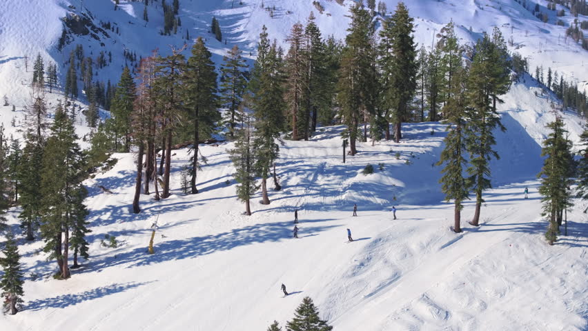 Group of friends skiing and snowboarding together down snowy mountain slope during snowfall at Palisades Tahoe, California USA. Lively winter sports atmosphere in alpine resort.
