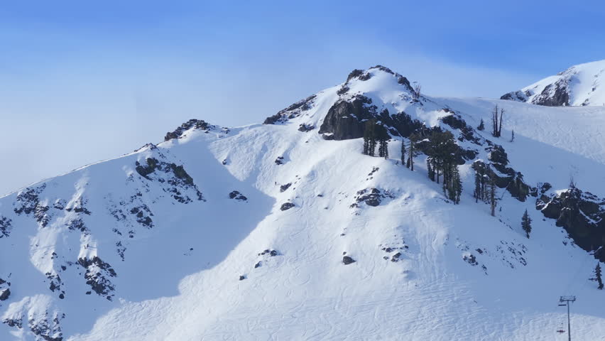 Group of skiers and snowboarders riding down alpine ridge in Palisades Tahoe, California USA. Snowy mountain landscape with dramatic winter sports motion.