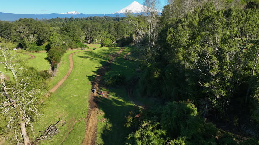 Aerial drone tracking shot of two ADV motorcycles riding on a dirt track in Los Lagos, Chile, with the snow-capped Osorno Volcano in the background.
