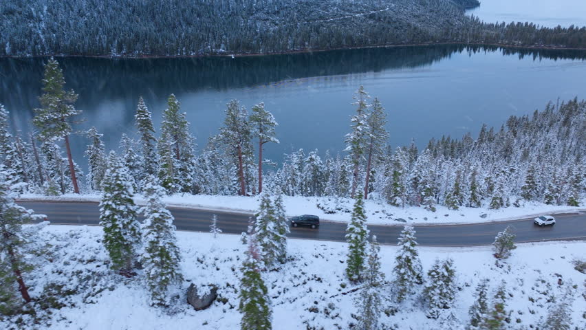Aerial drone view of Emerald Bay Road running along snowy shoreline with pine trees and deep blue water of Lake Tahoe. Fresh winter snow and alpine scenery. Emerald Bay, Lake Tahoe, California, USA.