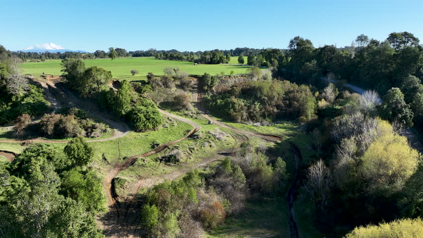 Aerial drone flying forward, approaching two ADV motorcyclists practicing on a winding dirt track in the scenic countryside of Los Lagos, Chile.