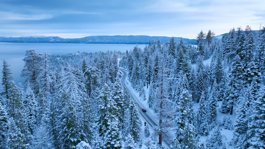 Aerial view of Emerald Bay Road winding through snow covered pine forest above Lake Tahoe. Scenic winter landscape blanketed in fresh snow. Lake Tahoe, California, USA.