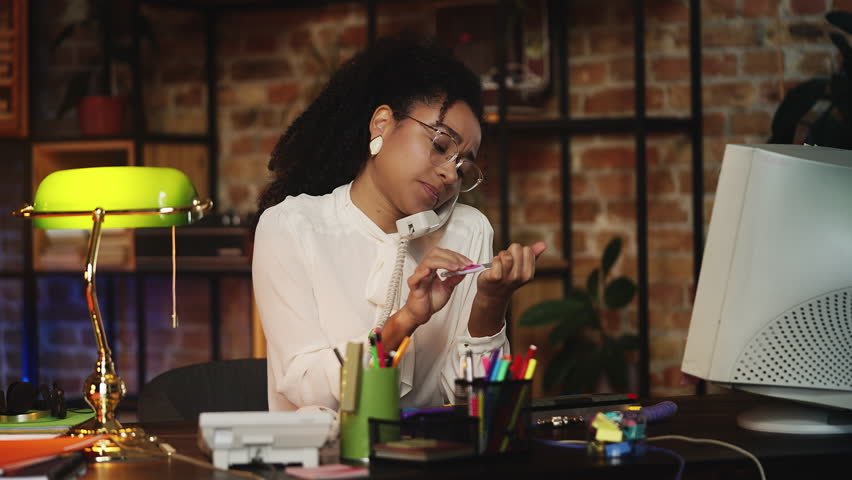 African American employee in retro clothes doing nails and talking on phone