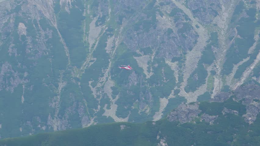 Rescue helicopter conducting operation over rugged mountain terrain