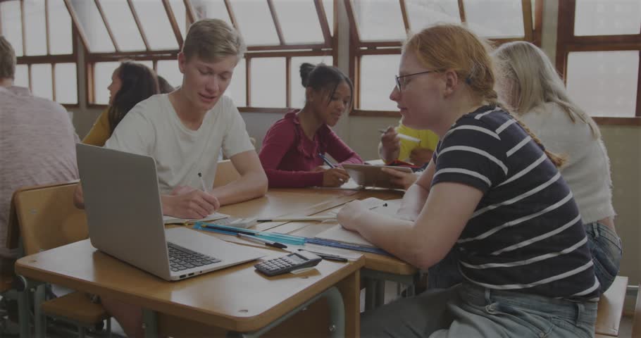 Male student pointing, peers writing and sharing laptop, waveform drifting, guiding school project. Collaboration, groupwork, classroom, students, desk, teamwork, learning