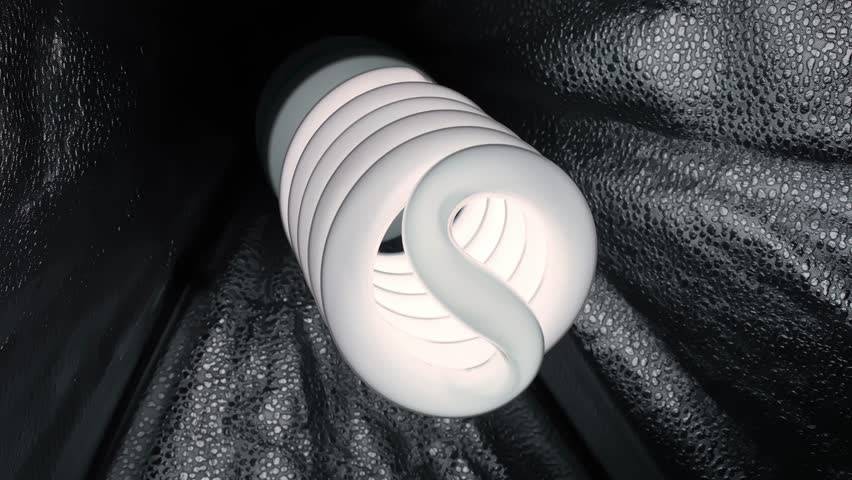 Close-up spiral CFL bulb on dark textured fabric with copy space, studio product shot concept for energy saving, lower electricity costs, and eco-friendly home efficiency.