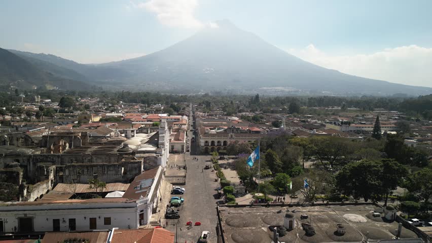 Aerial of Guatemalan flag and central park in Antigua Guatemala with hazy sky and Volcan Agua