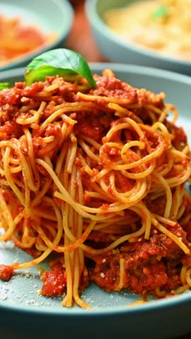 Spaghetti bolognese twirled on fork with tomato meat sauce. Close up of pasta noodles with red bolognese sauce and basil leaf on blue plate