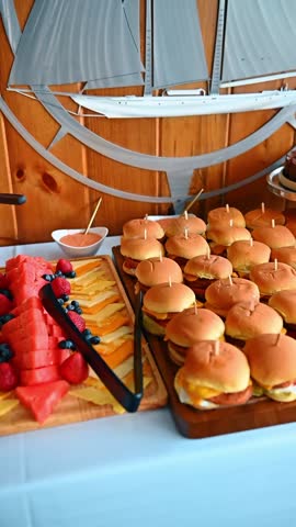 Mini cheeseburger sliders with toothpicks on wooden serving board. Rows of small beef burgers with melted cheese on buffet table