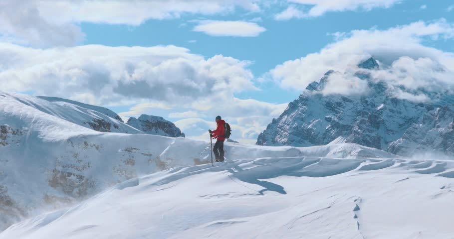 Aerial footage of a ski mountaineer ascending a snowy alpine ridge in Dolomites. Winter landscape, backcountry adventure, and solitude in breathtaking mountain scenery captured in 4K.