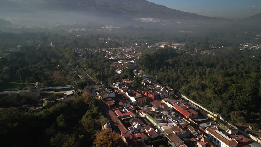 Aerial Antigua Guatemala pan up from colorful homes to Volcan Agua with hazy sky