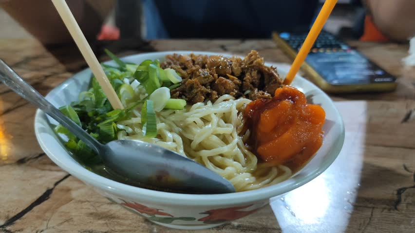 Hand Mixing Chicken Noodles in Bowl at Local Eatery