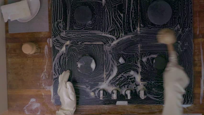 Overhead shot of female hands washing black glass cooktop with soap foam. Domestic cleaning routine, modern kitchen interior