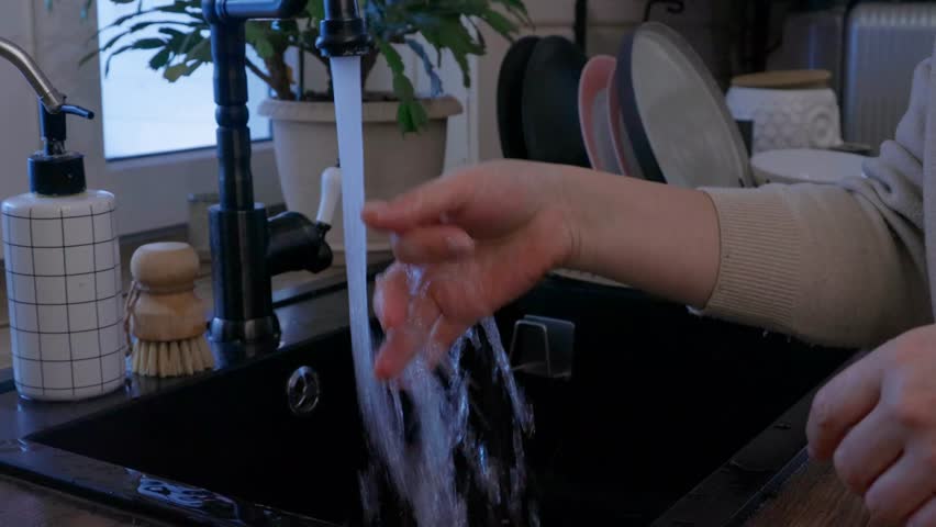 Top view of woman washing dishes in black kitchen sink. Everyday household chore in modern white kitchen interior. Domestic routine and kitchen hygiene concept