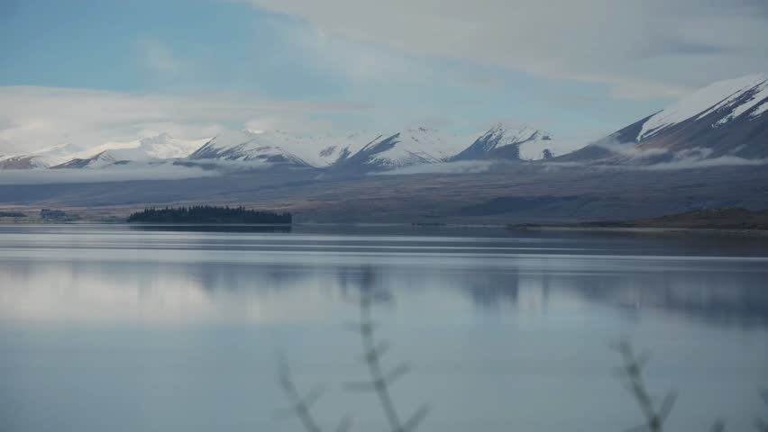 A dreamy and pastoral view of a snow capped mountains and their reflections, on a calm water lake at twilight. a 4K video clip, lake Tekapo, New Zealand.