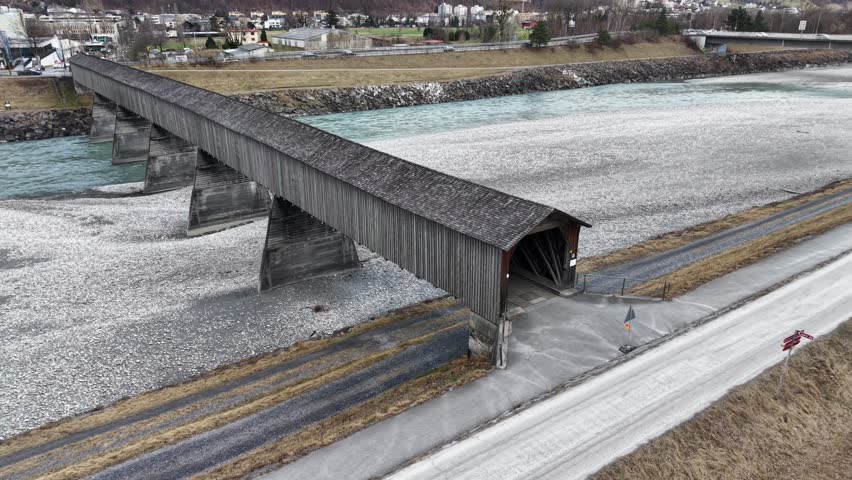 Static drone shot of cyclist exiting wooden pedestrian and bicycle bridge onto bike path, everyday commuting and active lifestyle scene