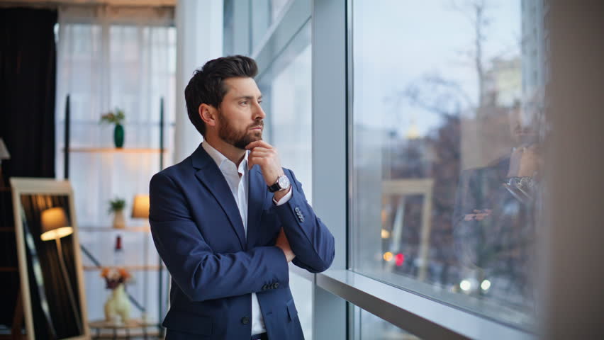 Thoughtful man standing big window hall closeup. Happy smiling entrepreneur businessman thinking idea startup corporate solution looking distance modern apartment. Positive ceo resting alone at work