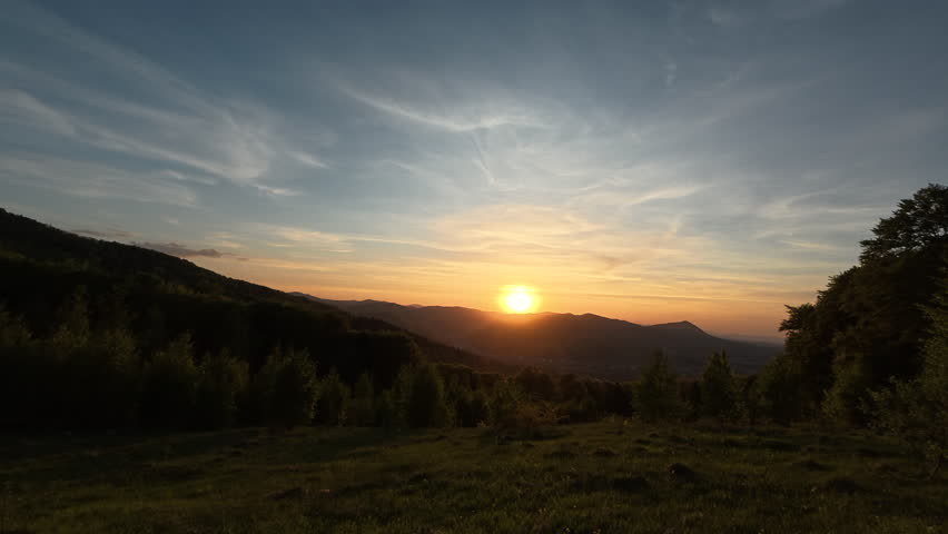 Majestic colorful cloudy sky over beautiful tops of hills. Amazing sunset moment. Landscape scenery of warm dusk sunset in mountains at summer time