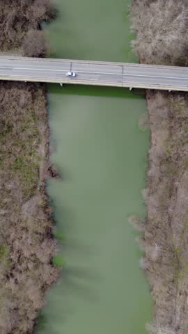 Vertical aerial top down view of a murky green river crossed by a bridge in early spring