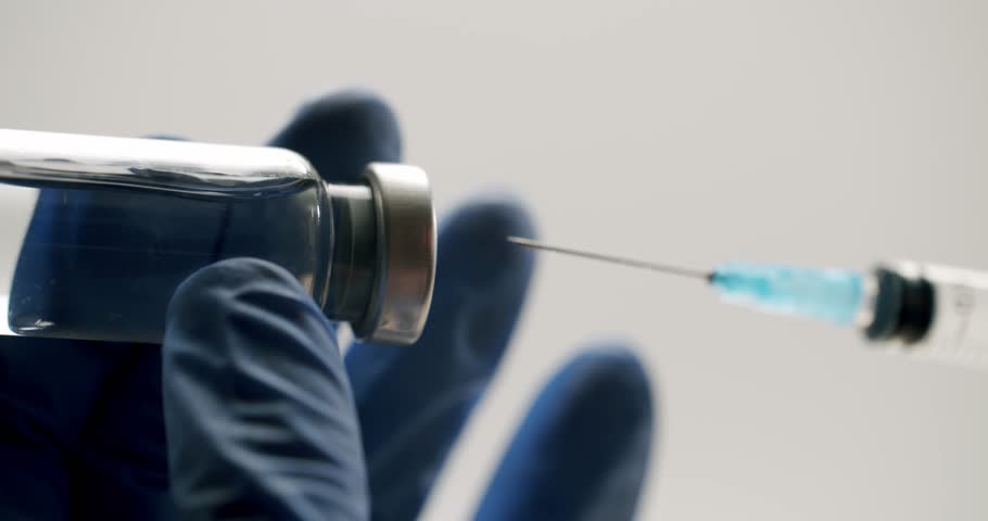 Medical professional in blue sterile gloves drawing a clear liquid vaccine from a glass vial into a syringe, preparing for an injection on an isolated white background in a hospital