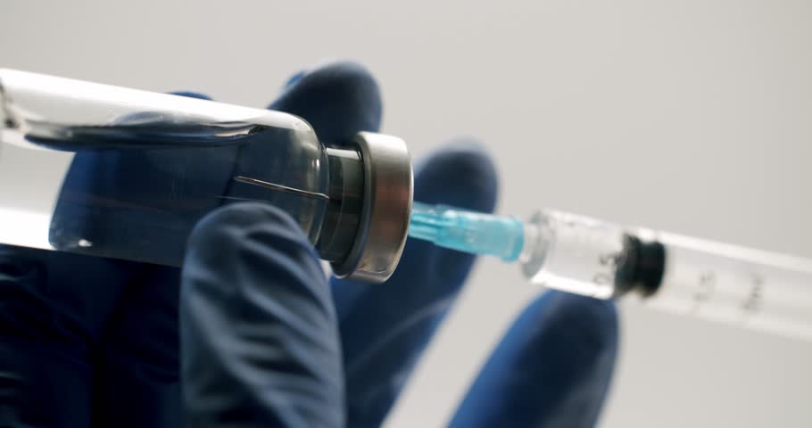 Medical professional in blue sterile gloves drawing a clear liquid vaccine from a glass vial into a syringe, preparing for an injection on an isolated white background in a hospital