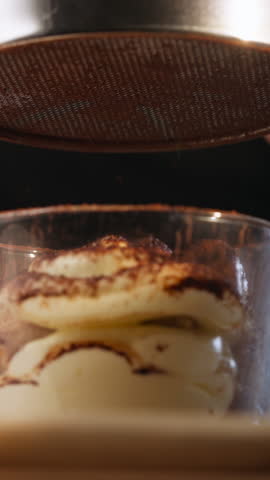 Dusting Cocoa Powder On Top Of Tiramisu Using Fine-Mesh Sieve. - vertical closeup shot